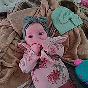 Gabriella is registered to the contest to win money with this photo: baby, infant, headband, bow, blanket, bedding, onesie, floral_pattern, hand, eyes, face, hat, plush_toy, toy, bed, cozy, pink_clothing, skirt, newborn, lying_down