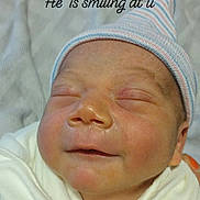 Kyng is registered to the contest to win money with this photo: newborn, baby, infant, smiling, sleeping, portrait, face, striped_cap, hat, white_clothing, blanket, swaddled, indoors, close_up, headshot, peaceful, cute, hospital, text_overlay, photograph