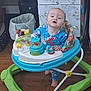 baby, child, walker, toy, blue_onesie, floor, wooden_floor, cabinet, trash_can, indoor, foot, face, person, furniture, colorful, plastic, playtime, curious, standing, home