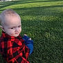 Christopher is registered to the contest to win money with this photo: baby, child, grass, park, outdoor, red_shirt, checkered_shirt, jeans, sitting, curious, sunlight, shadow, nature, green, casual_clothing, young_child, person, daylight, lawn, scenery