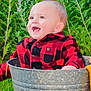 baby, checkered_shirt, child, cute, garden, grass, greenery, happy, metal_bucket, nature, outdoor, plants, playful, portrait, purple_flowers, red_shirt, sitting, smile, sunlight, young_child