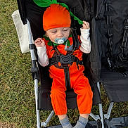 Kohen is registered to the contest to win money with this photo: baby, babywearing, carrot_costume, child, costume, cute, fall, grass, green, hat, leaf, orange, outdoor, pacifier, playful, portrait, seatbelt, socks, stroller, toddler