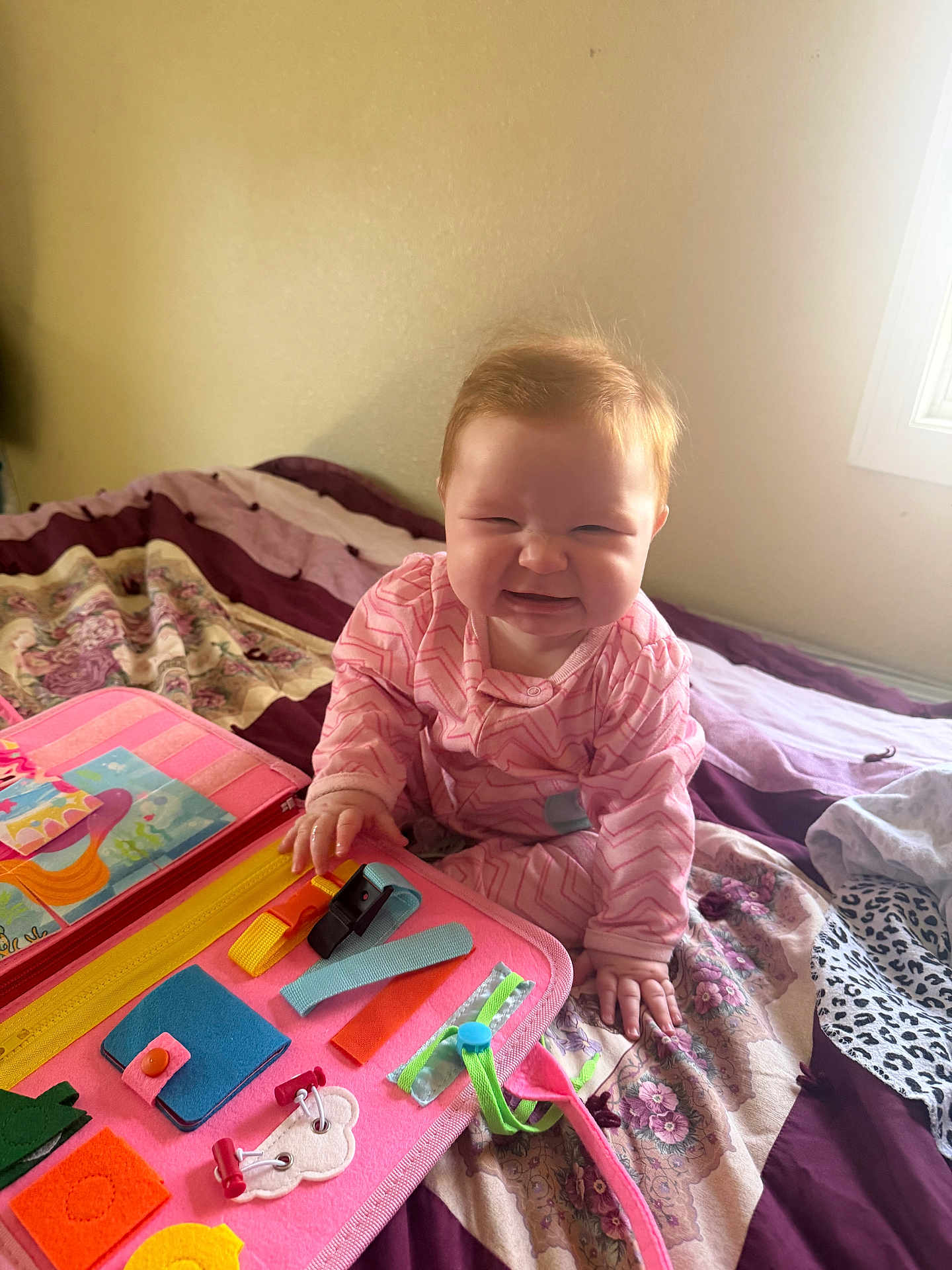 Lillian joined the competition — help win amazing prizes! baby, child, pajamas, bed, quilt, toy, busy_board, pink, purple, floral_pattern, hand, face, smile, indoor, window, light, playing, furniture, person, cute