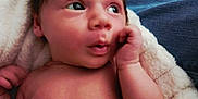 Milani is registered to the contest to win money with this photo: baby, blanket, child, cozy, curious, expression, eyes, face, hair, hand, indoor, infant, lap, newborn, patterned_background, person, portrait, skin, soft, young