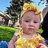 Vivian is registered to the contest to win money with this photo: baby, child, yellow_clothing, headband, outdoor, grass, tree, building, sunlight, person, face, expression, summer, nature, casual, jeans, adult, greenery, portrait, skin
