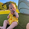 baby, child, keys, yellow_clothing, sunflower_pattern, outdoor, playground, slide, grass, green_turf, blue_sky, sunlight, sitting, barefoot, cute, infant, playing, chewing, happy, nature