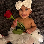 Jocelyn is registered to the contest to win money with this photo: baby, child, tutu, white_bow, rose, flower, smile, tongue_out, bare_chest, gold_necklace, earrings, soft_blanket, cute, portrait, infant, happy, lying_down, playful, adorable, accessories