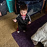 adidas, black_tracksuit, carpet, carpeted_floor, child, clothing, curious, floor, furniture, home, indoor, laundry_basket, person, playpen, purple_rug, room, small_object, standing, toddler, toy
