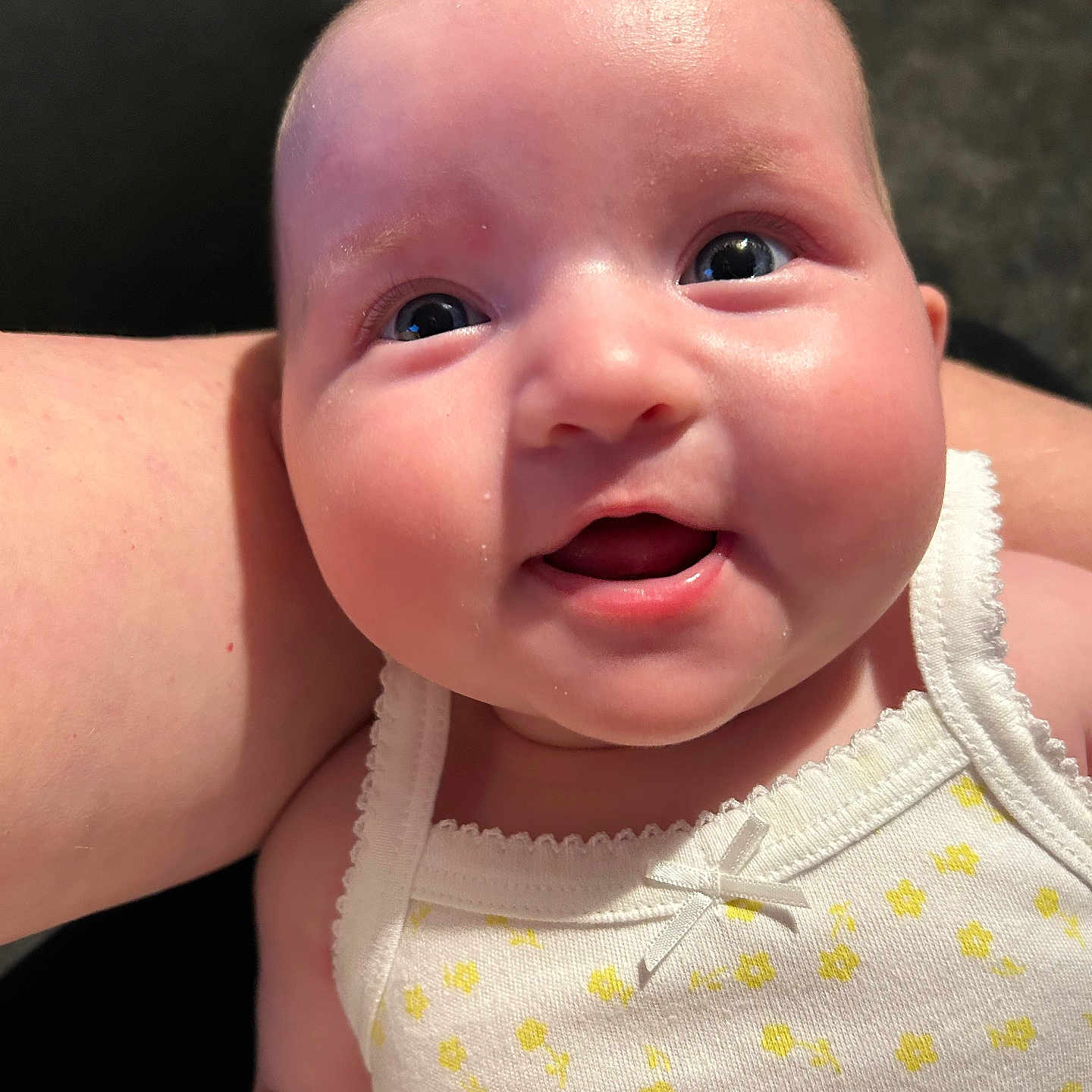 Siennarose is registered to the contest to win money with this photo: arm, baby, child, close_up, cute, expression, eyes, face, happy, human, indoors, infant, joyful, person, portrait, skin, smile, tank_top, white_clothing, yellow_flowers