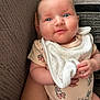 baby, infant, blue_eyes, onesie, bib, hand, couch, cushion, pattern, fabric, close_up, smile, skin, person, cute, child, indoor, soft_toy, holding, pink_dots