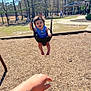 child, toddler, swing, playground, park, baby_swing, smile, happy, parent_hand, wood_chips, trees, sunny, outdoor, play, grass, person, daylight, recreation, casual_clothing, fun