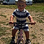toddler, child, balance_bike, outdoor, sunny, grass, dirt, van, shorts, striped_shirt, sandals, toy, play, person, summer, nature, park, young_child, bike, fun