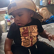 Bobby joined the competition — help win amazing prizes! toddler, child, cap, backwards_cap, black_tshirt, peace_sign, sitting, bed, indoor, furniture, bottle, container, curtain, shelf, plastic_bag, clothing, person, young_child, casual, room