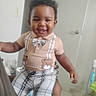 toddler, child, smiling, indoor, plaid_shorts, suspenders, teddy_bear, bow_tie, happy, person, face, curly_hair, short_sleeve_shirt, door, hand, floor, wall, baby, clothing, holding