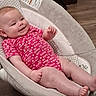 baby, infant, onesie, pink_clothing, smiling, baby_seat, cushion, face, skin, foot, hand, relaxing, wood_floor, indoor, comfort, child, cute, happy, young, person