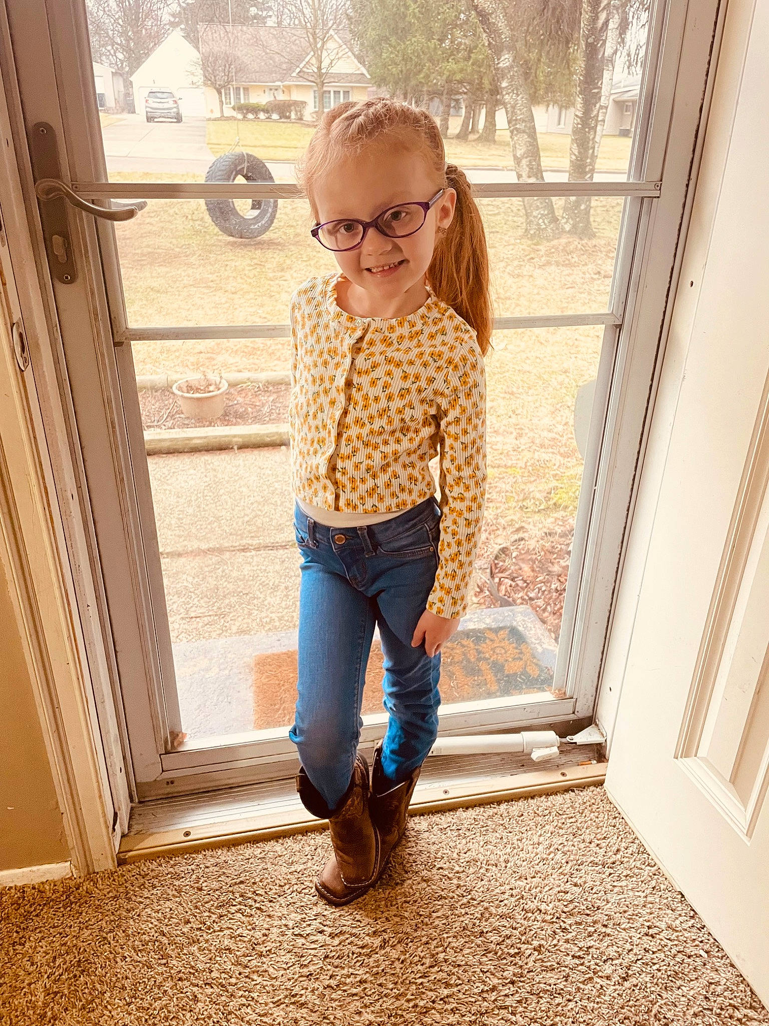 Emma is registered to the contest to win money with this photo: denim, electric_blue, eyewear, flooring, glasses, happy, human_body, human_leg, joy, knee, long_hair, pattern, person, sleeve, standing, textile, thigh, tints_and_shades, toddler, vision_care