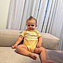 baby, child, infant, onesie, couch, sofa, curtains, indoor, smile, happy, face, person, legs, feet, hand, hairstyle, mohawk, fabric, home, furniture