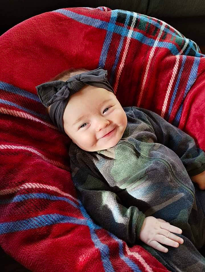 Lucinda is registered to the contest to win money with this photo: baby, baby_toddler_clothing, cheek, child, comfort, couch, eye, happy, headwear, joy, lap, linens, magenta, pattern, person, plaid, room, sitting, sleeve, smile