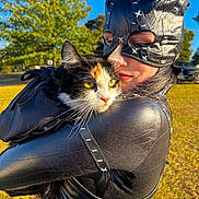 Tarot joined the competition — help win amazing prizes! person, cat, costume, calico_cat, outdoor, daylight, greenery, tree, grass, blue_sky, portrait, animal, pet, black_costume, leather, face, holding, closeup, sunlight, nature