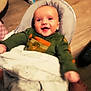 Jax joined the competition — help win amazing prizes! baby, child, smiling, blanket, green_shirt, dog_print, cushioned_seat, floor, wooden_floor, indoor, happy, person, face, infant, clothing, blanket_texture, foot, bottle, container, household_items