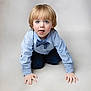 child, boy, blonde_hair, blue_eyes, bow_tie, crawling, cute, expression, face, hands, kneeling, light_blue_shirt, neutral_background, pants, playful, portrait, shirt, tongue_out, young, studio_photo