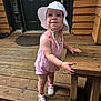 toddler, child, hat, romper, pink, white, shoes, socks, wooden_porch, bench, outdoor, standing, curious, baby, footwear, summer_clothing, door, planks, daylight, person