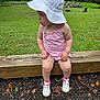 toddler, child, white_hat, pink_dress, outdoor, grass, wooden_beam, nature, greenery, shoes, sitting, curious, forest, leaves, summer, daylight, young_child, cute, casual, playful