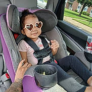 Za'Riyah is registered to the contest to win money with this photo: toddler, child, car_seat, heart_shaped_sunglasses, purple, tattoo, hand, car_interior, seatbelt, smiling, window, tree, building, grass, cup_holder, casual_clothing, safety, sunlight, portrait, happy