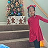 Za'Layah is registered to the contest to win money with this photo: child, girl, red_dress, red_bows, braided_hair, staircase, carpet, christmas_tree, ornaments, gingerbread_decorations, snowman_figure, holiday, decorations, indoor, family_photos, wall_art, holiday_season, festive, smiling, pose