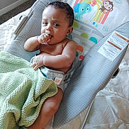 Ethan joined the competition — help win amazing prizes! baby, infant, blanket, baby_seat, sitting, hand_in_mouth, curious, indoor, quilt, clothing, striped_socks, face, child, person, cute, comfort, soft, colorful, pattern, furniture