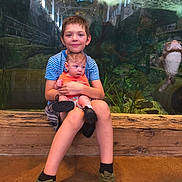Riley is registered to the contest to win money with this photo: children, baby, boy, siblings, aquarium, fish, underwater, portrait, sitting, holding, smiling, family, wooden_bench, striped_shirt, orange_clothing, sneakers, indoor, zoo, aquatic_life, photography