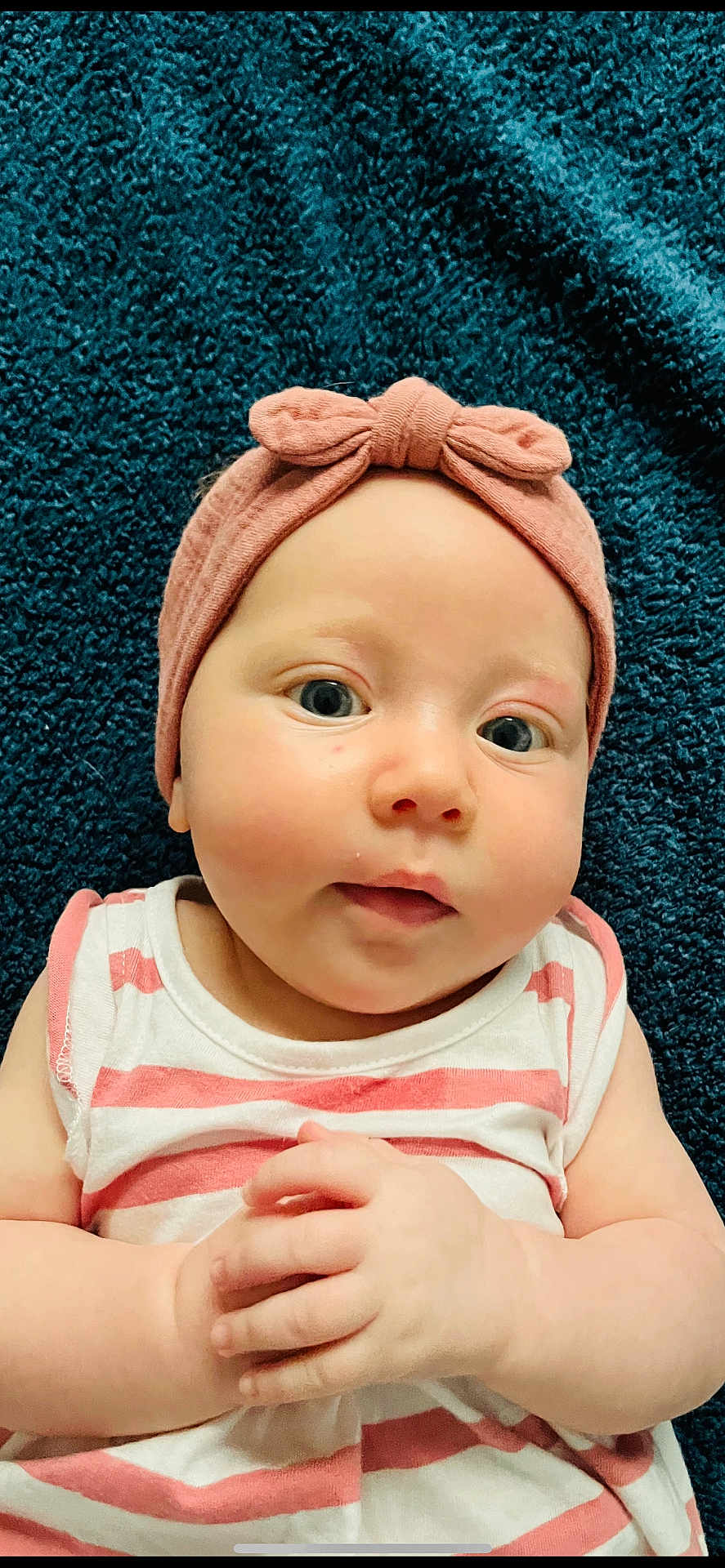 Louise a rejoint le concours — aidez-le/la à gagner de superbes lots ! baby, infant, headband, bow, pink, striped_clothing, hands, face, eyes, skin, cheeks, lying_down, blanket, blue_background, closeup, portrait, cute, child, soft_texture, expression