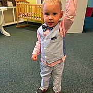 Joey is registered to the contest to win money with this photo: toddler, child, boy, indoor, carpet, clothing, vest, bow_tie, striped_pants, shoes, crib, adult_hand, room, wall, floor, furniture, portrait, standing, cute, holding_hand