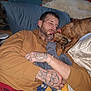 man, adult_male, sleeping, dog, brindle_dog, pet, bed, pillow, blanket, tattoos, hand, beard, cuddle, stuffed_animal, pajamas, bracelet, cozy, indoor, portrait, resting