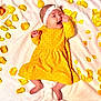 baby, birthday_candle, blanket, cake, celebration, cute, face, festive, foot, hand, happy, headband, indoors, infant, lying_down, portrait, rose_petals, smiling, soft_texture, yellow_dress