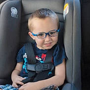 Jace is registered to the contest to win money with this photo: child, car_seat, glasses, smiling, seatbelt, plaid_shorts, tshirt, car_interior, young_child, sitting, safety, happy, boy, window, daylight, headrest, seat, casual_clothing, travel, road_trip