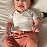 baby, child, smiling, white_top, peach_pants, bow, hair_accessory, cushion, baby_clothing, infant, happy, cute, portrait, indoors, soft_texture, relaxed, feet, hands, young_child, person