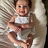 baby, child, smile, blue_eyes, purple_bow, white_dress, eyelet_fabric, barefoot, infant, soft_blanket, portrait, happy, cute, lying_down, indoors, skin, hair, person, closeup, young_child
