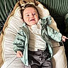 baby, child, smiling, jacket, clothing, lying_down, cushion, hair_clip, cute, happy, indoor, infant, portrait, person, apparel, fabric, young_child, comfortable, expression, face