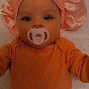Alani joined the competition — help win amazing prizes! baby, infant, pacifier, bonnet, orange_clothing, laying_down, face, eyes, sleepwear, child, cute, young, portrait, indoors, blanket, pattern, bird_pattern, headwear, small_child, baby_girl