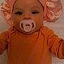 baby, infant, pacifier, bonnet, orange_clothing, laying_down, face, eyes, sleepwear, child, cute, young, portrait, indoors, blanket, pattern, bird_pattern, headwear, small_child, baby_girl