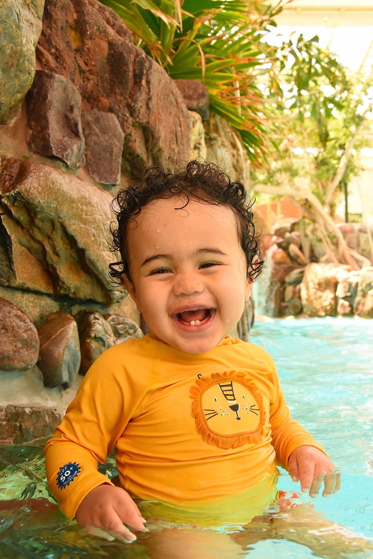 Kyan a rejoint le concours — aidez-le/la à gagner de superbes lots ! toddler, child, smiling, water, pool, yellow_shirt, curly_hair, happy, outdoor, rocks, greenery, sitting, splashing, sunlight, swimwear, cute, young_child, water_fun, portrait, playful
