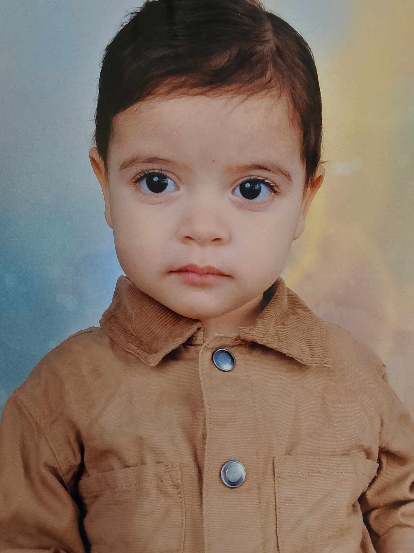 Anes participe au concours pour gagner de l'argent avec cette photo : child, toddler, face, portrait, brown_jacket, button, curly_hair, young, serious_expression, studio_background, close_up, person, indoor, cute, eyelashes, skin, head, clothing, buttoned_jacket, small_child