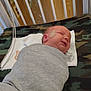 newborn, baby, swaddled, sleeping, crib, hospital, medical_patch, blanket, towel, camouflage, infant, bed, wooden_bars, resting, cute, small, face, person, indoors, healthcare