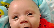 Tyson is registered to the contest to win money with this photo: baby, infant, face, smile, eyes, blanket, blue_blanket, red_shirt, bed_sheet, cartoon_bear, closeup, happy, child, portrait, indoors, soft_texture, cute, expression, head, person