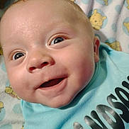 Tyson joined the competition — help win amazing prizes! baby, infant, smile, face, close_up, blue_shirt, text_on_clothing, blanket, cartoon_bear, happy, wide_eyes, cute, child, portrait, indoors, soft_texture, skin, human, head, expression