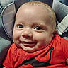 Tyson joined the competition — help win amazing prizes! baby, infant, smile, face, red_shirt, seat, straps, blue_background, wide_eyes, cute, portrait, child, expression, indoor, clothing, person, head, happy, closeup, babywearing
