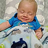 baby, smiling, blanket, blue_clothing, pillow, cloud_pattern, infant, sleeping, cozy, cute, child, soft_toy_pattern, happy, indoors, portrait, person, bedtime, snuggled, peaceful, resting