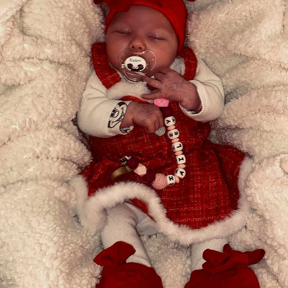Haïley a rejoint le concours — aidez-le/la à gagner de superbes lots ! baby, infant, sleeping, red_bow, red_dress, white_blanket, pacifier, beaded_toy, booties, cozy, cute, festive, holiday, newborn, child, clothing, soft_texture, indoor, portrait, adorable
