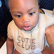 Truce is registered to the contest to win money with this photo: baby, child, infant, cute, bib, chain, pacifier, tattoo, hand, skin, clothing, sitting, indoor, table, closeup, face, expression, young, adorable, person